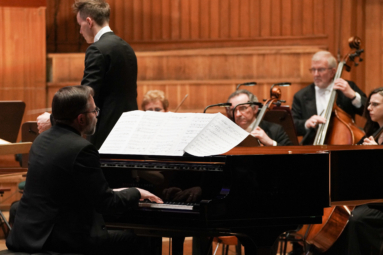 zdjęcie mężczyzny grającego na fortepianie, w tle dyrygent i orkiestra