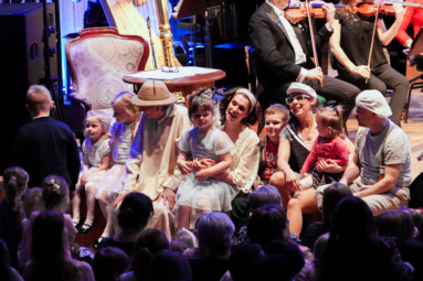 zdjęcie aktorów siedzących na estradzie, trzymających na kolanach dzieci, z którymi wspólnie wykonują piosenkę