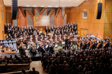 orkiestra, dyrygent, chór i tubafony na estradzie wykonują dzieło Pendereckiego