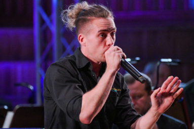 zdjęcie młodego mężczyzny z kitką na głowie i mikrofonem w ręku