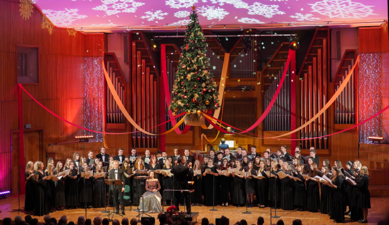zdjęcie chóru i solistów podczas świątecznego koncertu na estradzie FP, nad którą wisi choinka