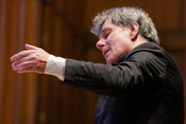 zdjęcie siwego dyrygenta kontemplującego muzykę z zamkniętymi oczami, z ręką uniesioną ku górze