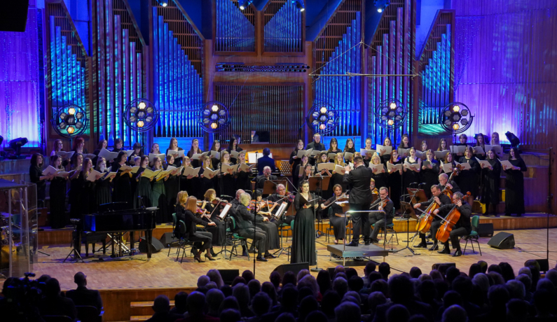 zdjęcie orkiestry kameralnej i chóru na estradzie filharmonii podświetlonej na niebiesko