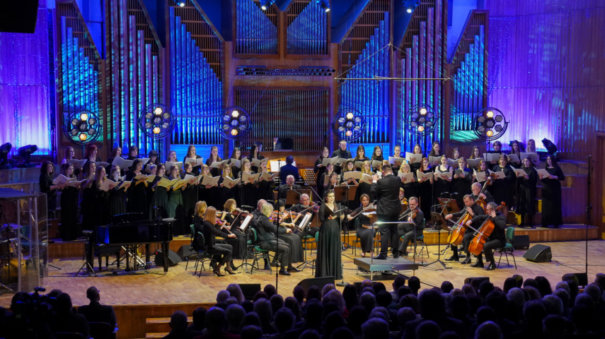 zdjęcie orkiestry kameralnej i chóru na estradzie filharmonii podświetlonej na niebiesko