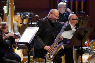 zdjęcie łysego pana w średnim wieku, grającego na saksofonie