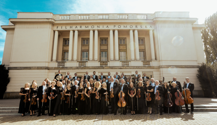 zdjęcie muzyków Orkiestry Symfonicznej FP stojących przed gmachem FP z instrumentami w rękach