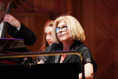 zdjęcie pianistki gającej na fortepianie, wpatrującej się ze skupieniem w dyrygenta