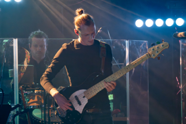 Muzyk we włosach spiętych w kitkę grający na gitarze elektrycznej.