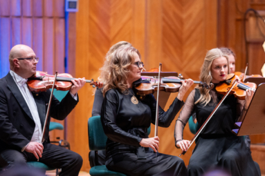 Troje muzyków, elegancko ubranych, gra na skrzypcach, koncentrując się na nutach.
