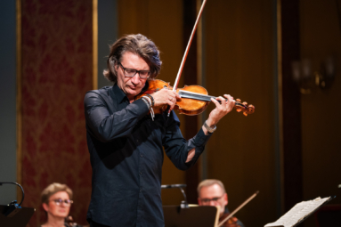 mężczyzna w długich włosach i okularach grający na skrzypcach z zamkniętymi oczami