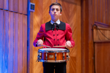 Chłopiec w czerwonym stroju gra w skupieniu na werblu.