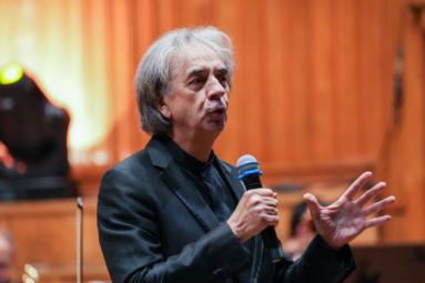 Mężczyzna w czarnym garniturze przemawia do mikrofonu na estradzie