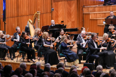 Orkiestra symfoniczna gra na estradzie, w tle harfa i fortepian.