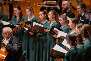 młode chórzystki w zielonych sukienkach śpiewające z nut, które trzymają w czarnych teczkach